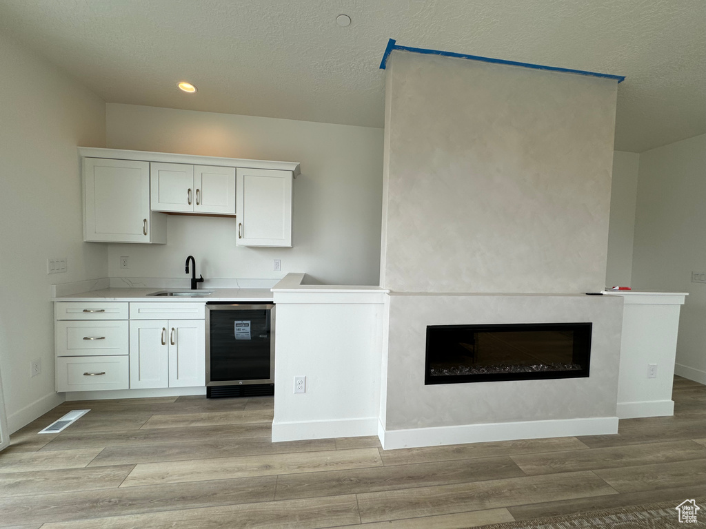 Kitchen featuring sink, light hardwood / wood-style flooring, beverage cooler, white cabinets, and a large fireplace