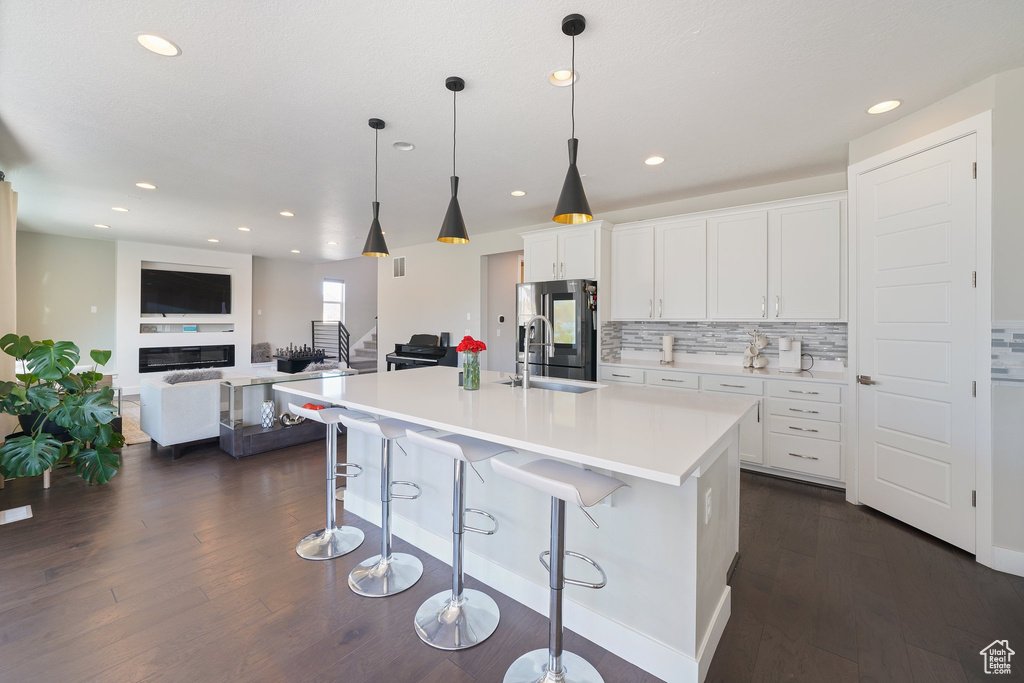 Kitchen with white cabinets, dark wood-type flooring, a breakfast bar area, pendant lighting, and stainless steel refrigerator
