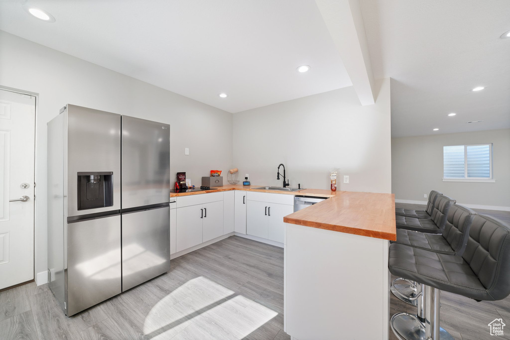 Kitchen with appliances with stainless steel finishes, kitchen peninsula, white cabinetry, and light hardwood / wood-style flooring
