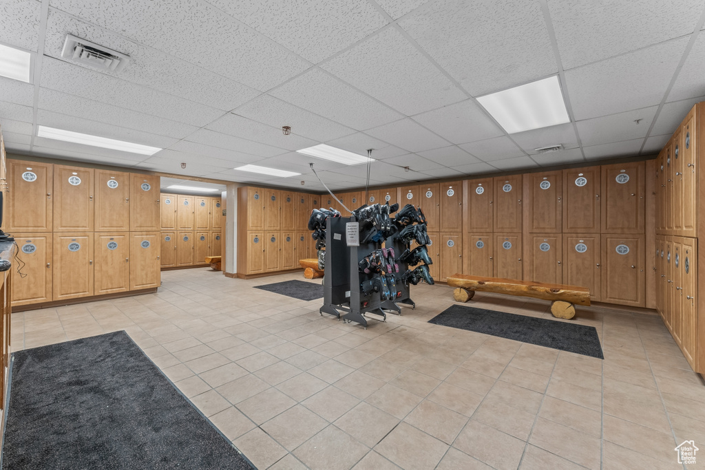 Workout room with light tile flooring, a paneled ceiling, and wooden walls
