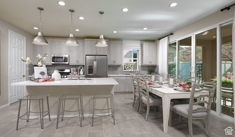 Kitchen with tasteful backsplash, appliances with stainless steel finishes, a kitchen island with sink, a breakfast bar area, and pendant lighting