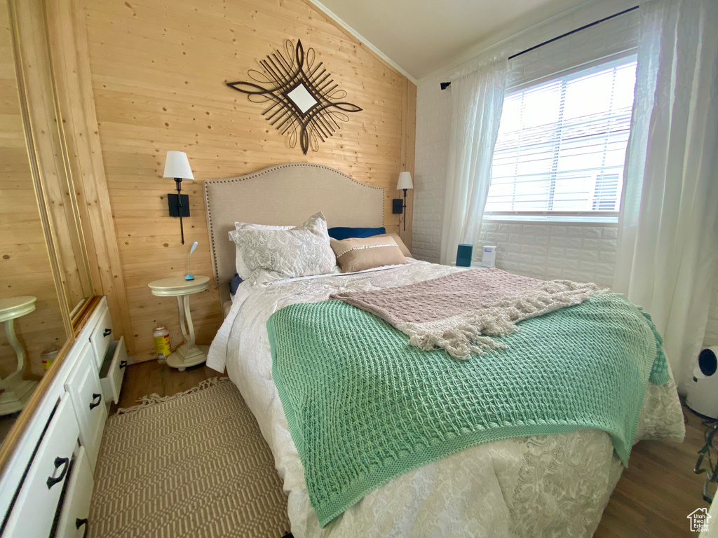 Bedroom with light hardwood / wood-style flooring, wooden walls, and vaulted ceiling