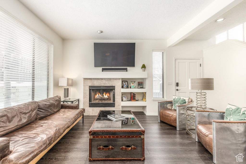 Living room featuring dark wood-type flooring, a wealth of natural light, a tile fireplace, and built in shelves