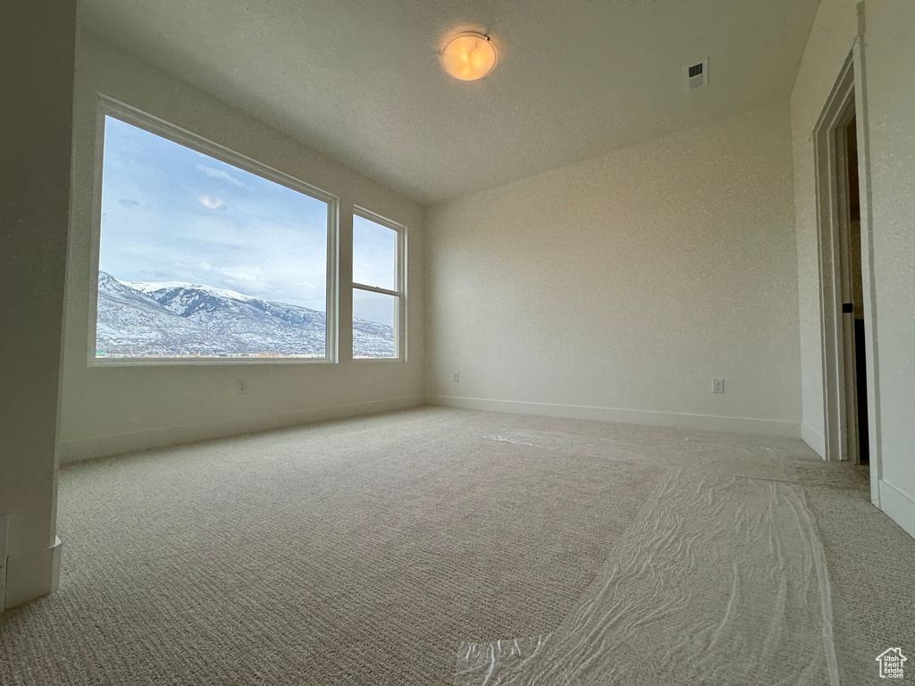 Empty room with vaulted ceiling, a mountain view, and light colored carpet