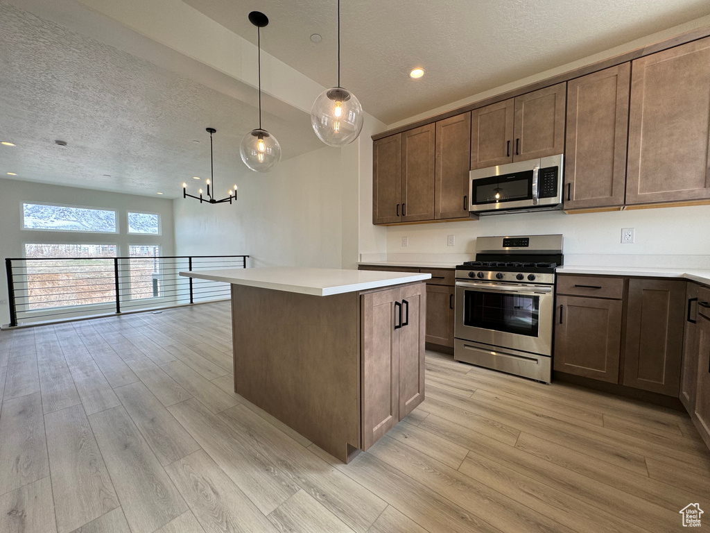 Kitchen featuring decorative light fixtures, light wood-type flooring, a center island, an inviting chandelier, and stainless steel appliances