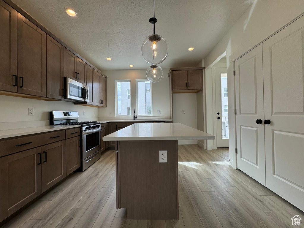 Kitchen featuring pendant lighting, light hardwood / wood-style flooring, a center island, dark brown cabinetry, and stainless steel appliances