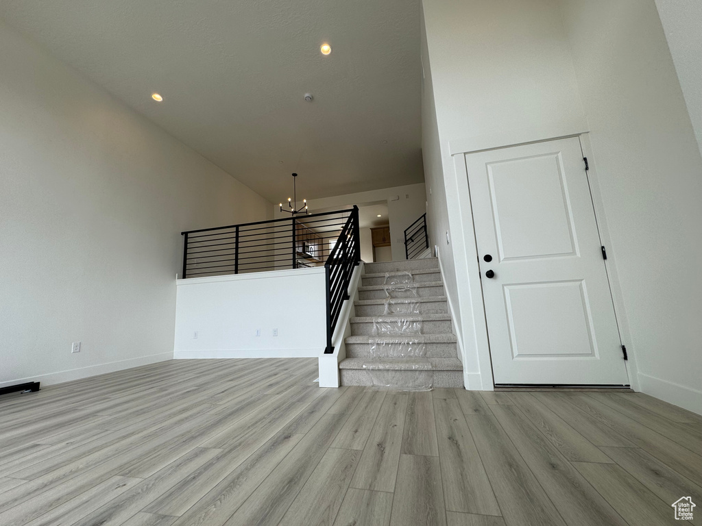 Staircase featuring an inviting chandelier, a towering ceiling, and light hardwood / wood-style floors