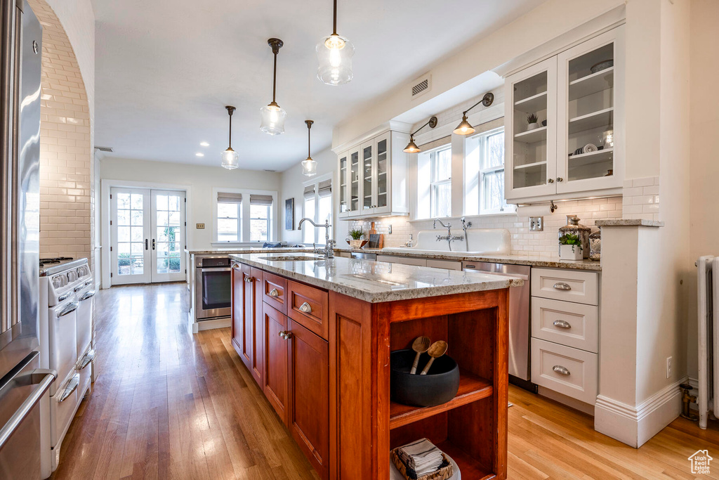 Kitchen with white cabinetry, pendant lighting, light hardwood / wood-style floors, an island with sink, and appliances with stainless steel finishes