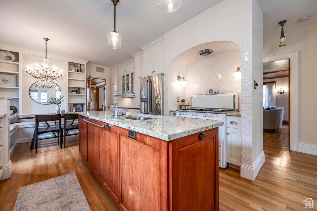Kitchen featuring a notable chandelier, a kitchen island with sink, light hardwood / wood-style floors, white cabinets, and high end fridge