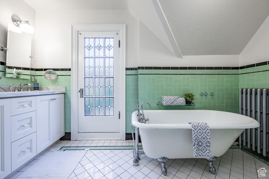Bathroom featuring a bathtub, radiator, vanity with extensive cabinet space, tile walls, and tile floors