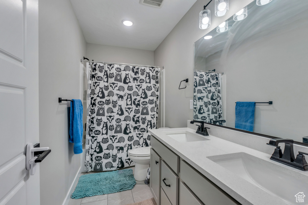 Bathroom featuring dual bowl vanity, toilet, and tile flooring