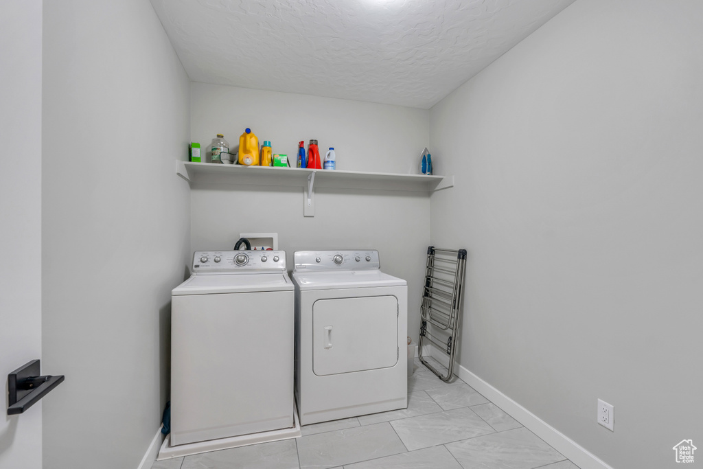 Laundry room with washer hookup, light tile floors, a textured ceiling, and washing machine and clothes dryer
