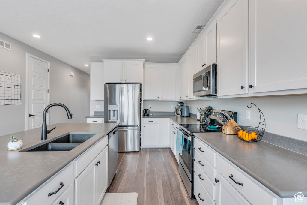 Kitchen with appliances with stainless steel finishes, a center island with sink, white cabinets, sink, and light hardwood / wood-style flooring