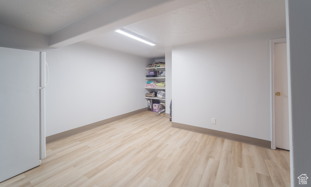 Basement with light wood-type flooring and white refrigerator
