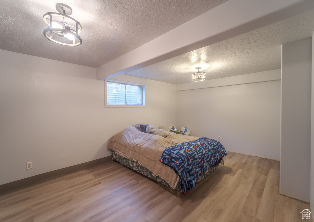 Bedroom with a textured ceiling, a notable chandelier, and light hardwood / wood-style floors
