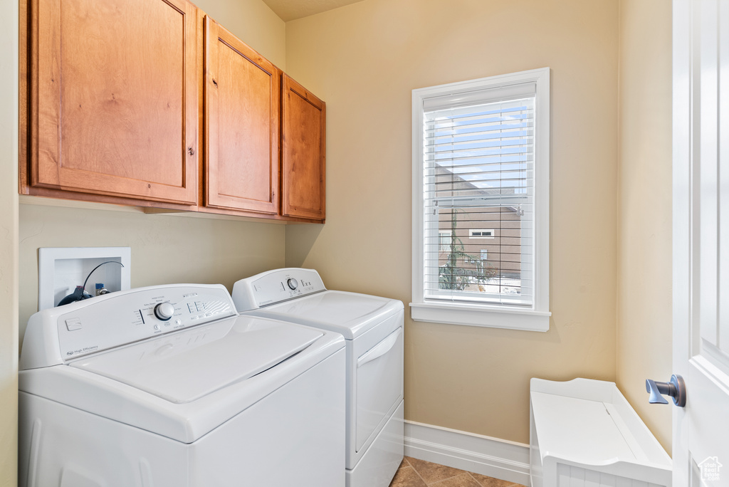 Clothes washing area with cabinets, light tile flooring, washer and dryer, and a healthy amount of sunlight