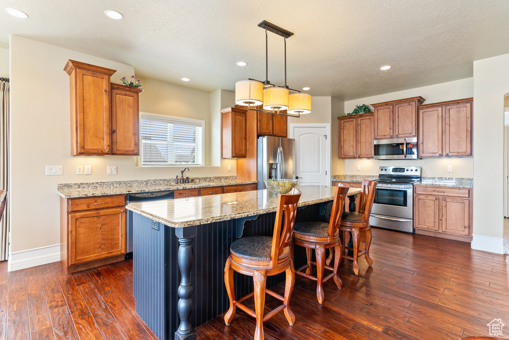 Kitchen with dark hardwood / wood-style flooring, a kitchen island, stainless steel appliances, and a breakfast bar area