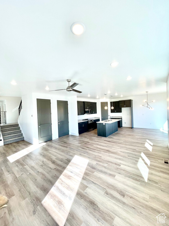 Unfurnished living room with sink, light hardwood / wood-style floors, and ceiling fan with notable chandelier