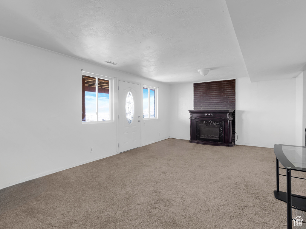 Unfurnished living room featuring brick wall, light carpet, and a fireplace