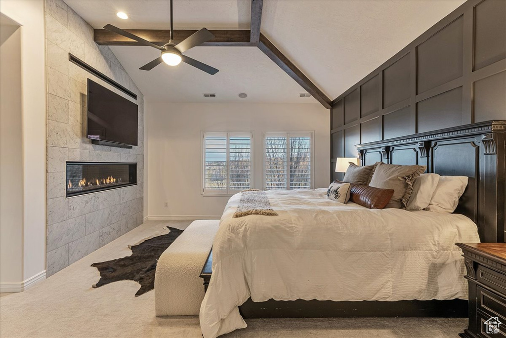 Carpeted bedroom featuring vaulted ceiling with beams, a tile fireplace, and ceiling fan