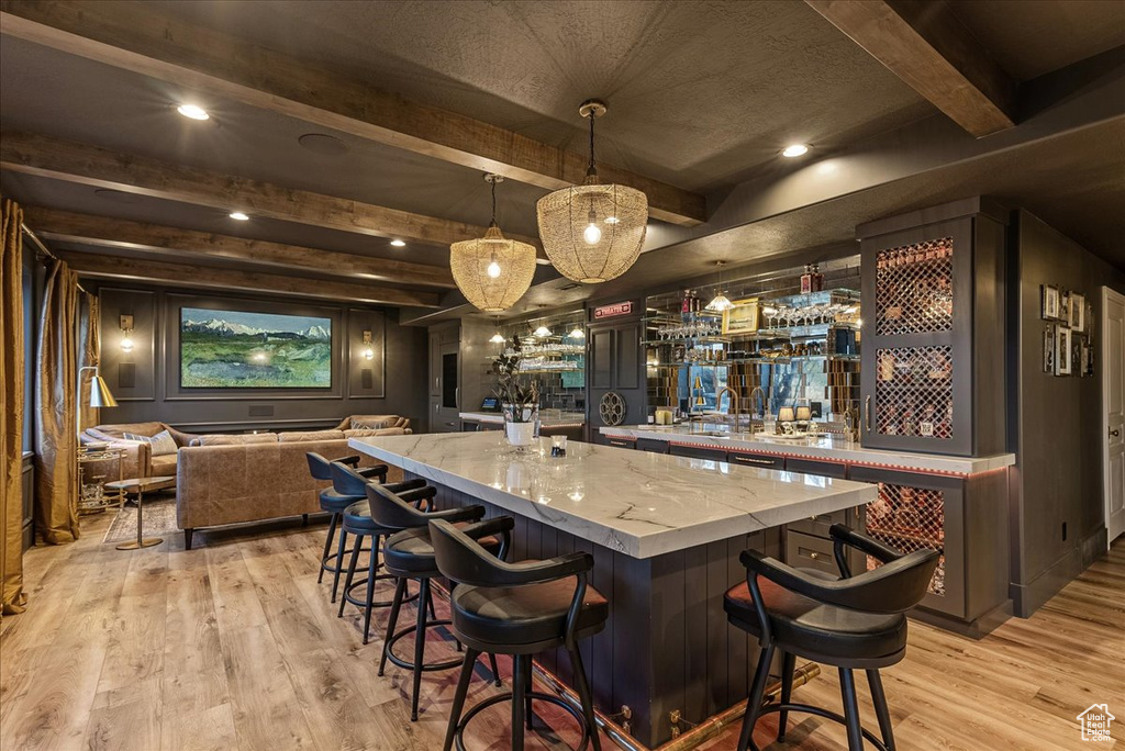 Bar with sink, pendant lighting, light hardwood / wood-style floors, beam ceiling, and light stone counters