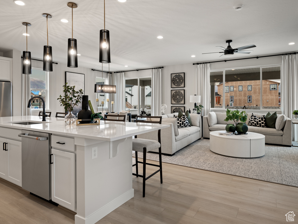 Kitchen featuring white cabinetry, an island with sink, ceiling fan, and hanging light fixtures