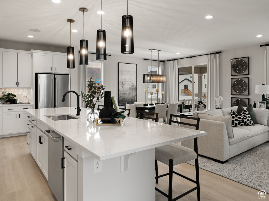 Kitchen featuring light hardwood / wood-style flooring, a center island with sink, a breakfast bar, stainless steel appliances, and pendant lighting