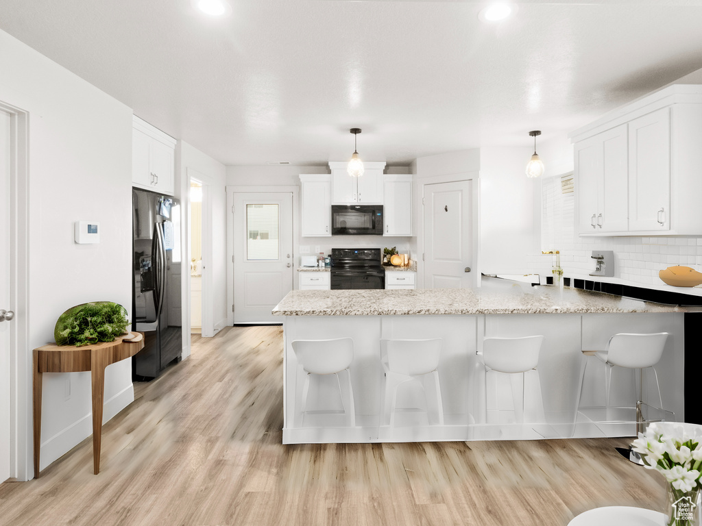 Kitchen with hanging light fixtures, light wood-type flooring, stainless steel fridge with ice dispenser, and range