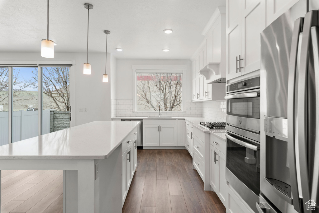 Kitchen with tasteful backsplash, appliances with stainless steel finishes, plenty of natural light, a center island, and hanging light fixtures