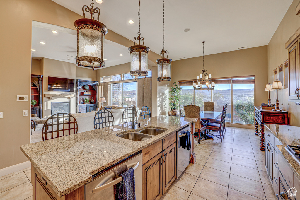 Kitchen with decorative light fixtures, an island with sink, light tile floors, dishwasher, and light stone counters