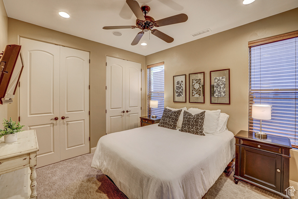 Bedroom with light colored carpet, multiple closets, and ceiling fan