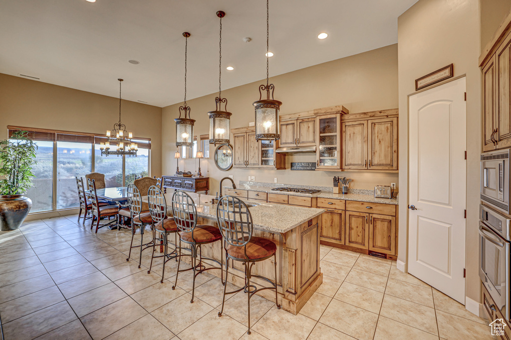 Kitchen with light stone countertops, a kitchen island with sink, decorative light fixtures, appliances with stainless steel finishes, and an inviting chandelier