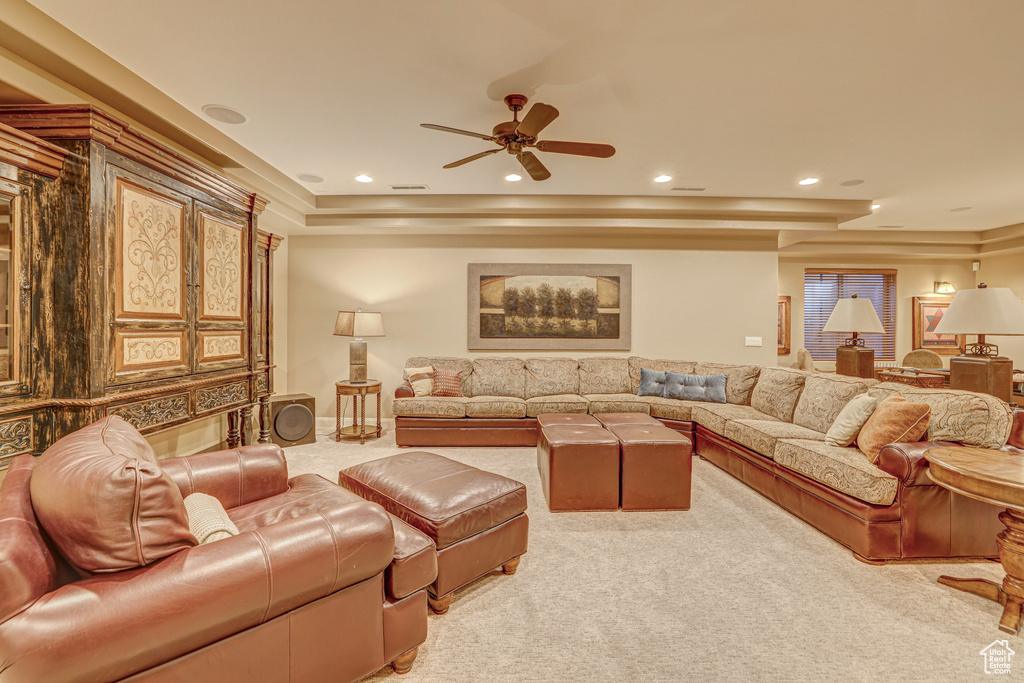 Living room with a raised ceiling, light colored carpet, and ceiling fan