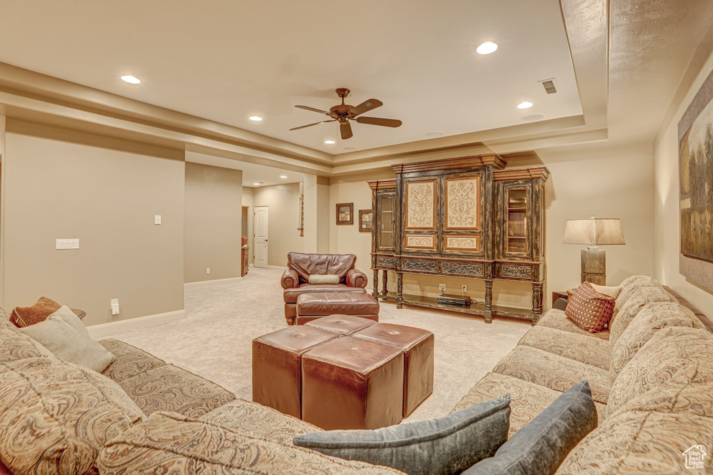 Living room featuring a raised ceiling, light colored carpet, and ceiling fan