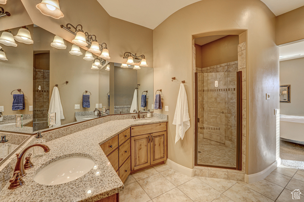 Bathroom with dual sinks, tile flooring, vanity with extensive cabinet space, and a shower with door