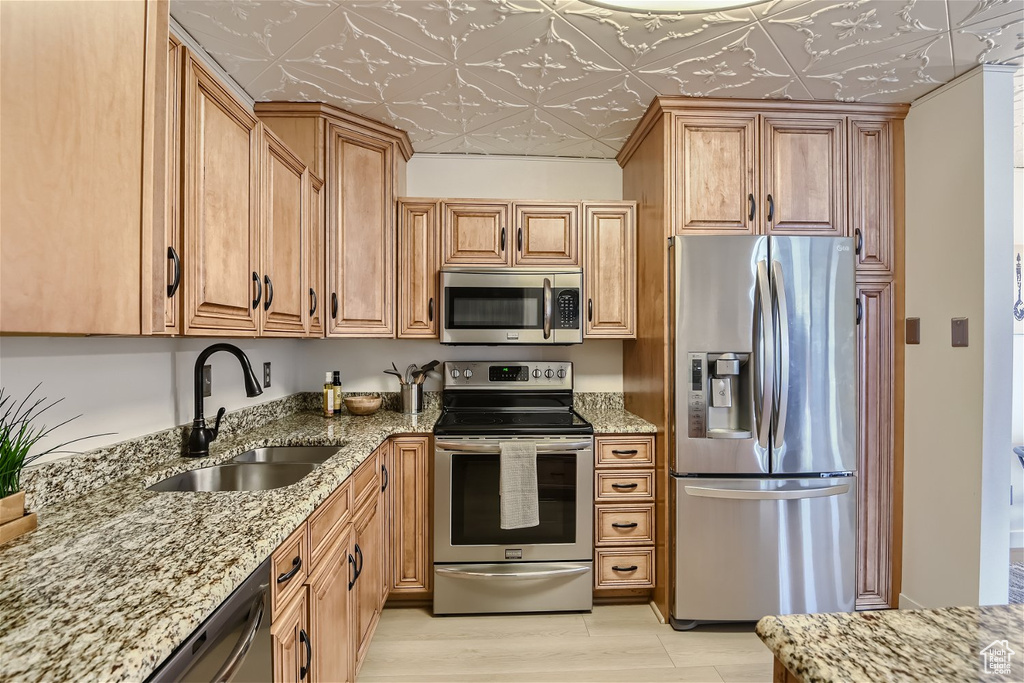 Kitchen featuring appliances with stainless steel finishes, light wood-type flooring, light stone countertops, and sink