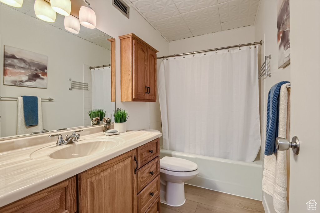 Full bathroom featuring hardwood / wood-style floors, large vanity, toilet, and shower / tub combo with curtain