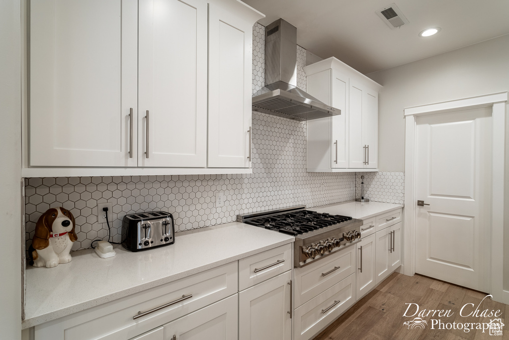 Kitchen featuring white cabinetry, backsplash, light hardwood / wood-style floors, and wall chimney range hood