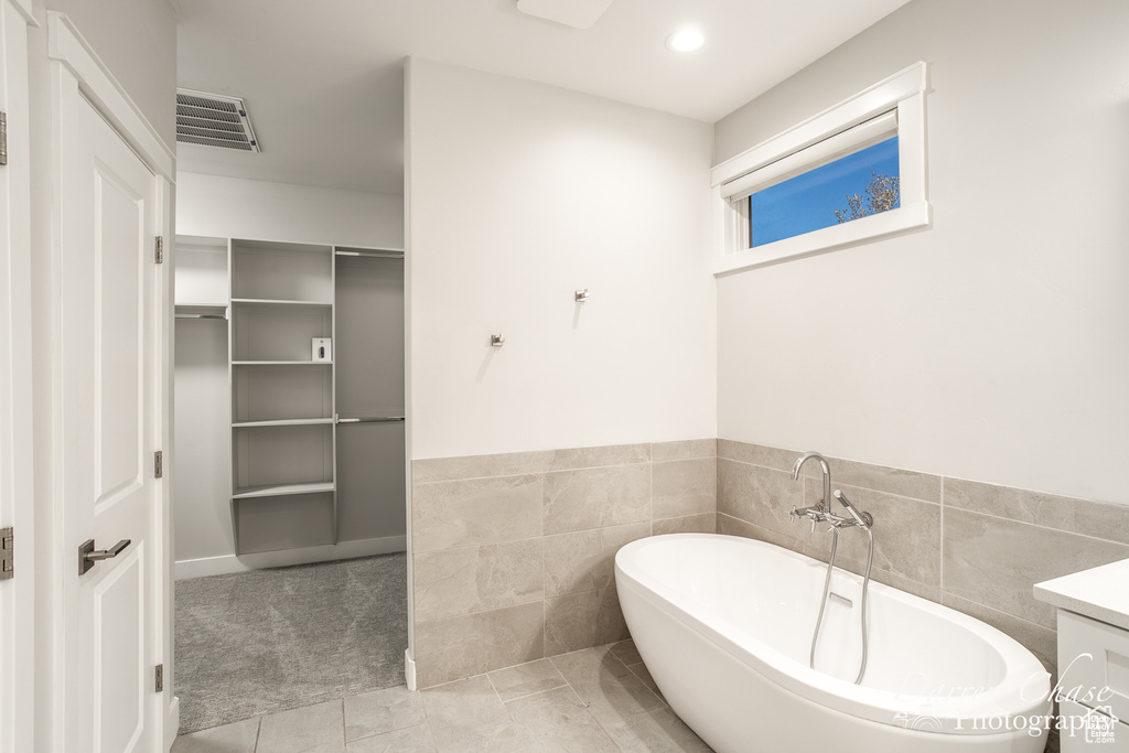 Bathroom featuring vanity, tile flooring, a bathtub, and tile walls