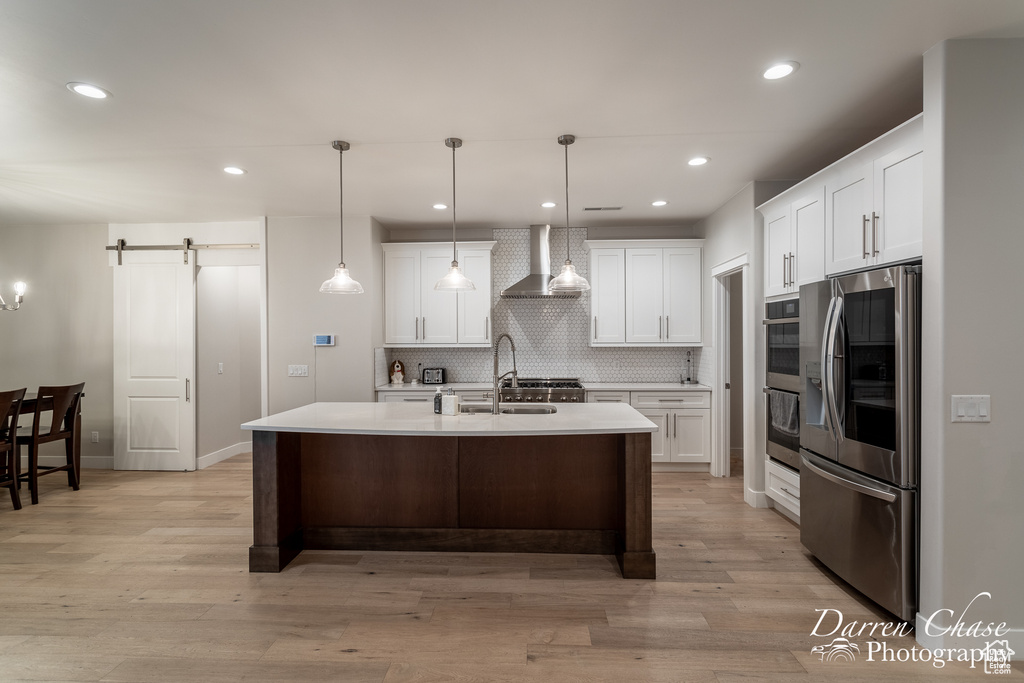 Kitchen featuring backsplash, a barn door, appliances with stainless steel finishes, light hardwood / wood-style floors, and wall chimney exhaust hood