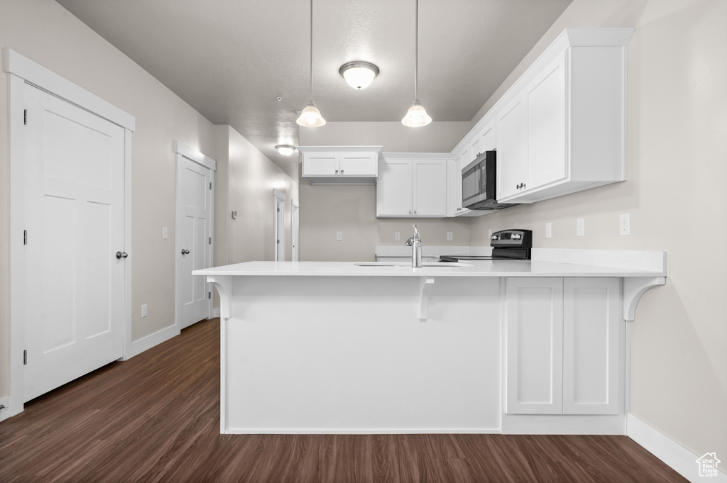 Kitchen with white cabinets, kitchen peninsula, range, dark hardwood / wood-style flooring, and decorative light fixtures
