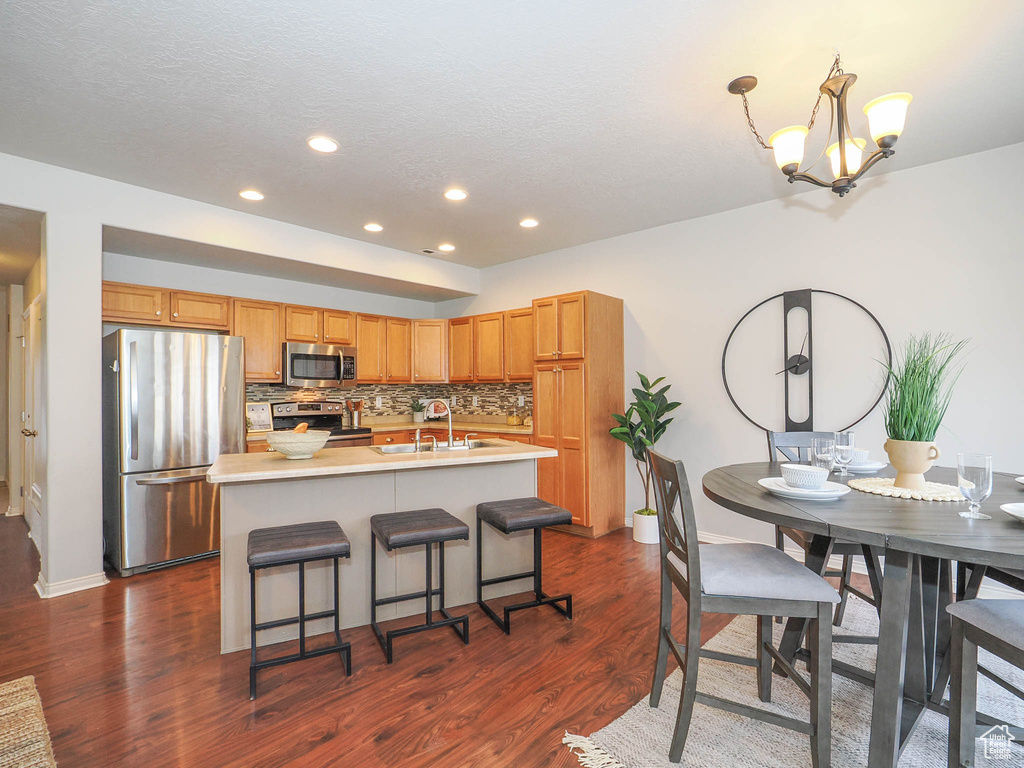 Kitchen with a notable chandelier, stainless steel appliances, a center island with sink, and dark wood-type flooring