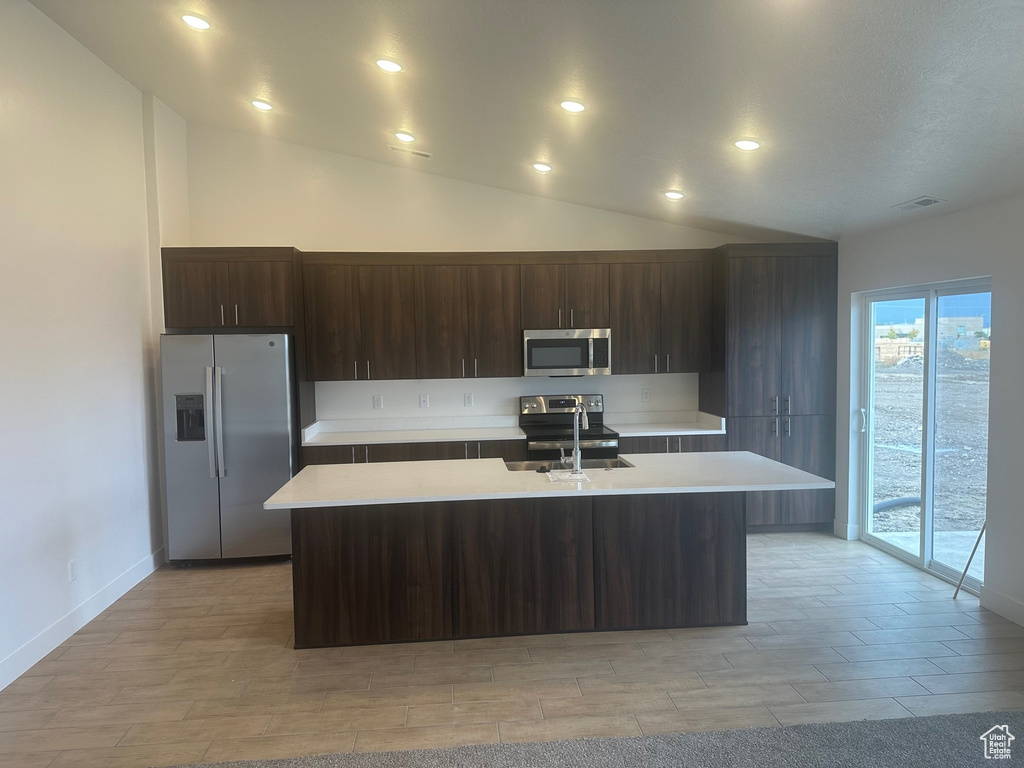 Kitchen featuring appliances with stainless steel finishes, dark brown cabinets, sink, and a center island with sink