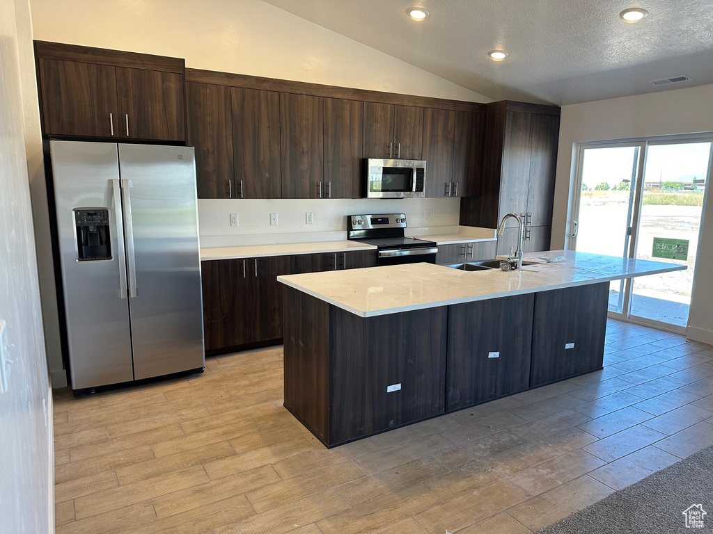 Kitchen with vaulted ceiling, a center island with sink, stainless steel appliances, sink, and light hardwood / wood-style flooring
