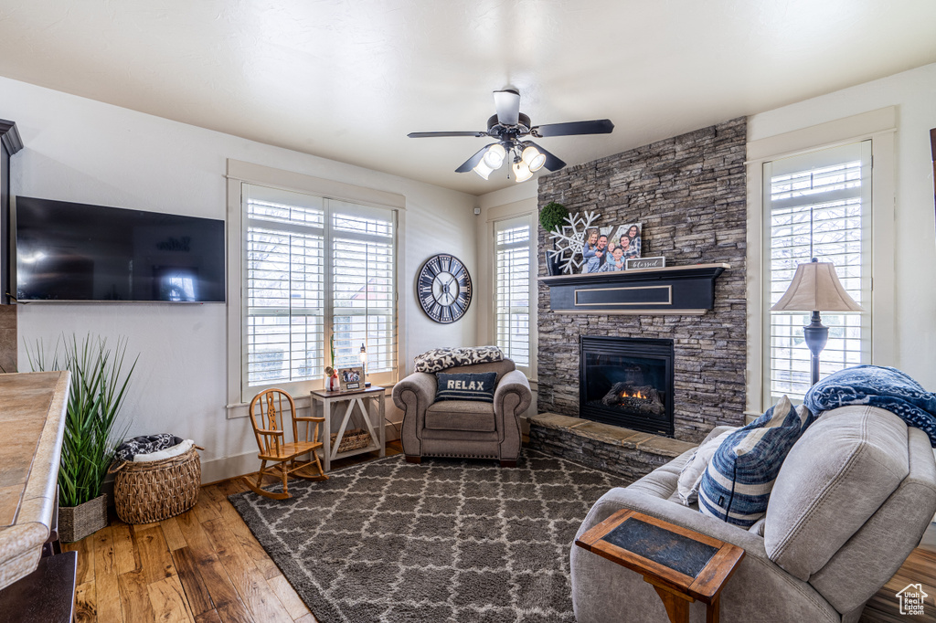 Living room with plenty of natural light, a stone fireplace, dark wood-type flooring, and ceiling fan