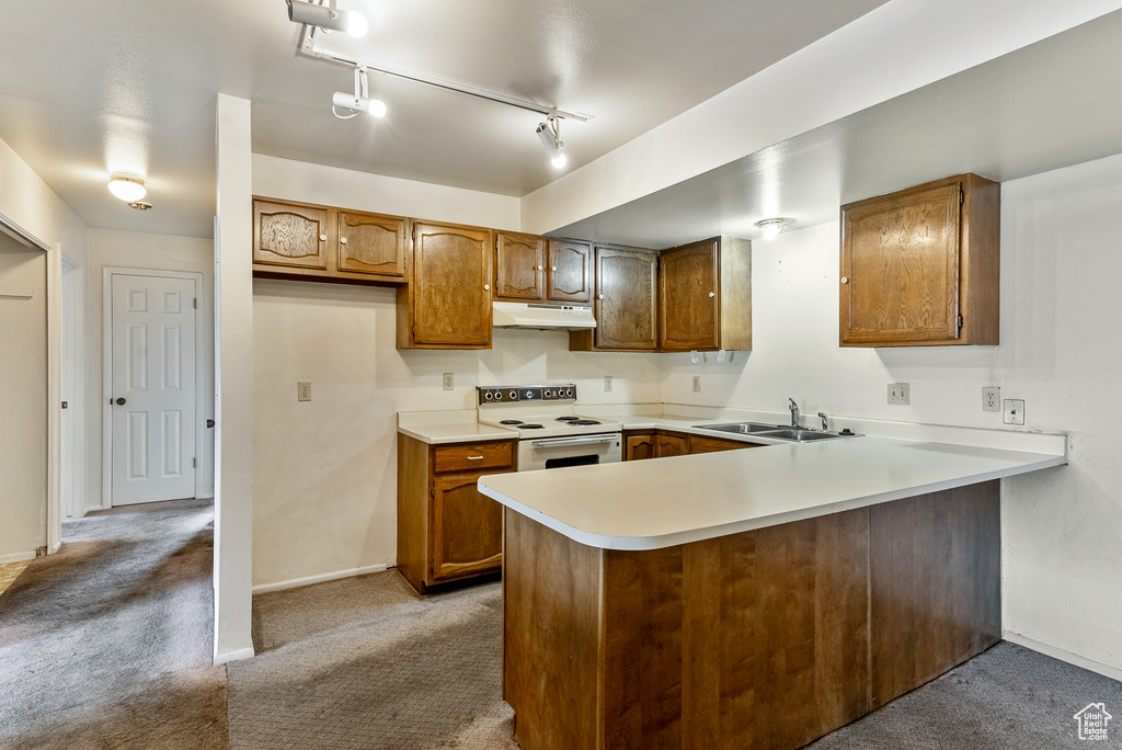 Kitchen with sink, kitchen peninsula, white electric range, rail lighting, and dark colored carpet