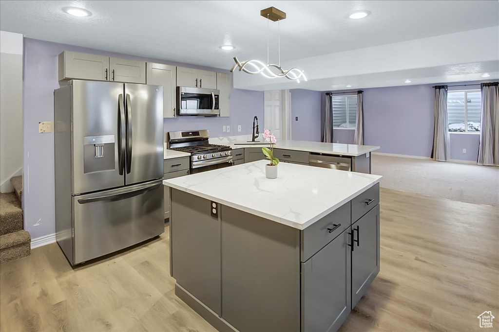 Kitchen with light carpet, gray cabinetry, appliances with stainless steel finishes, a kitchen island, and decorative light fixtures