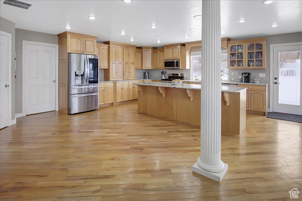 Kitchen featuring decorative columns, appliances with stainless steel finishes, a kitchen breakfast bar, a kitchen island, and light wood-type flooring