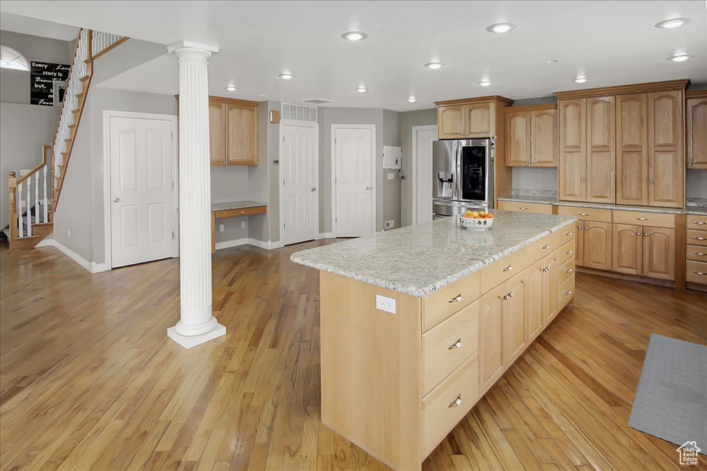 Kitchen featuring decorative columns, a center island, stainless steel fridge, light wood-type flooring, and light stone counters