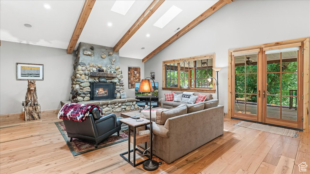 Living room featuring a fireplace, light hardwood / wood-style floors, beam ceiling, and a skylight